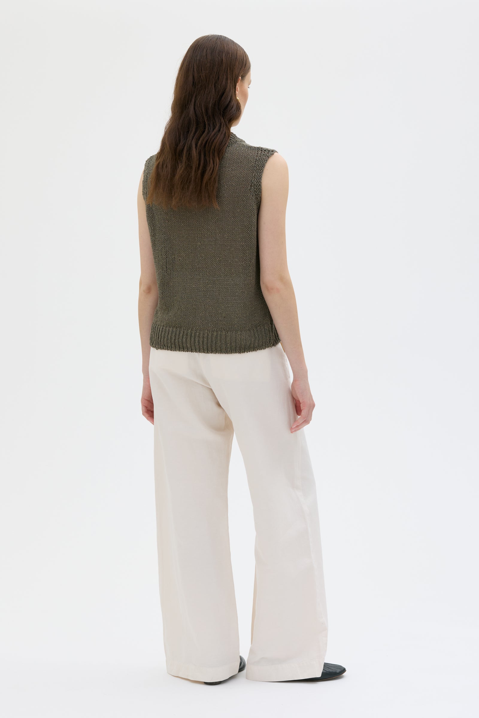 Person wearing a green sleeveless sweater and white pants on a white background