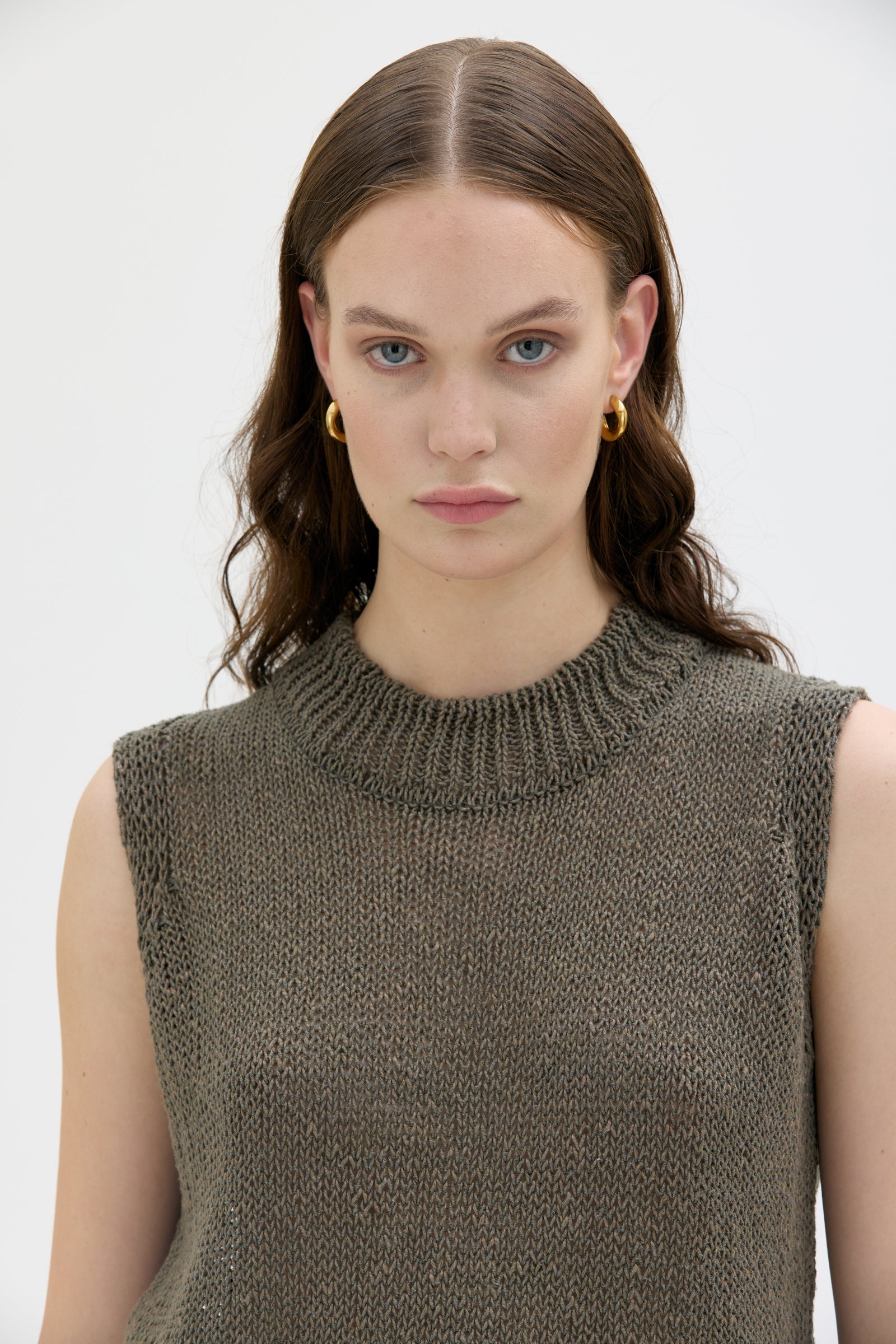 Woman wearing a brown knitted sleeveless top against a white background