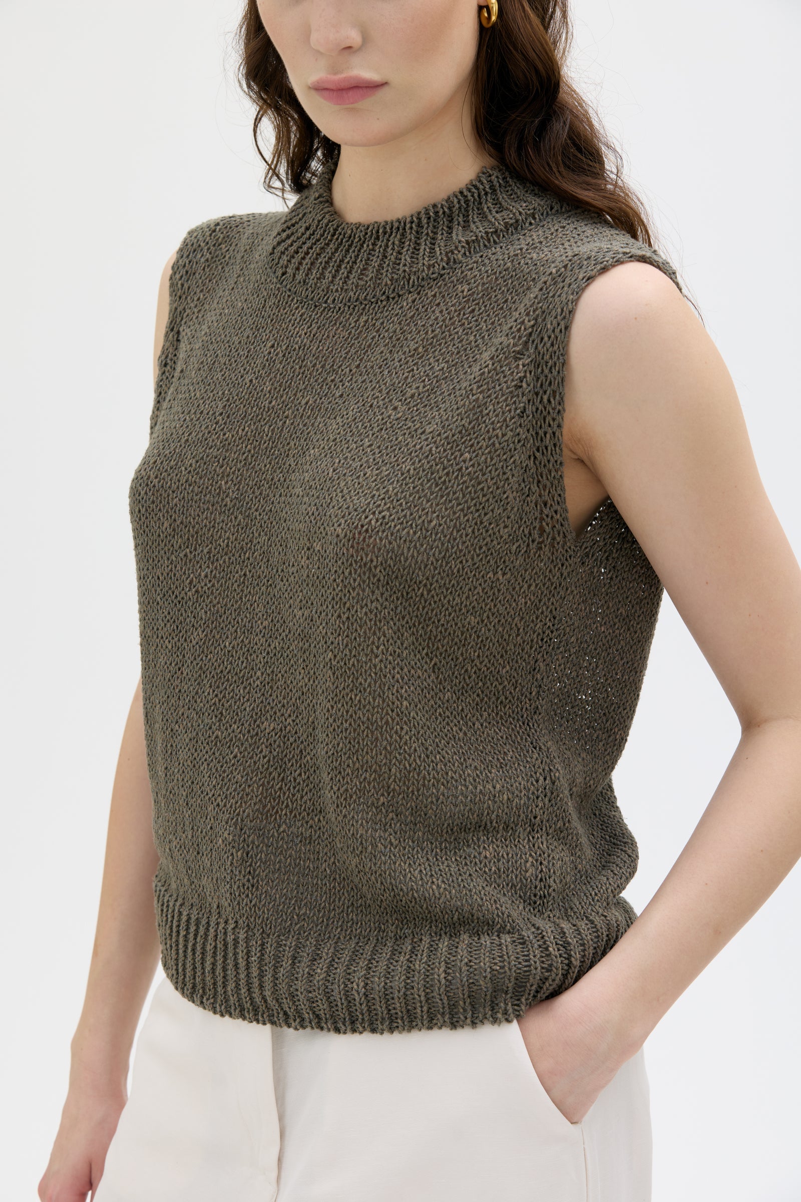 Woman wearing a sleeveless knitted sweater against a plain background