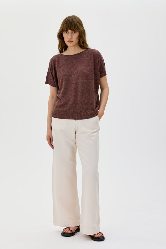 Woman wearing a brown top and white pants on a white background
