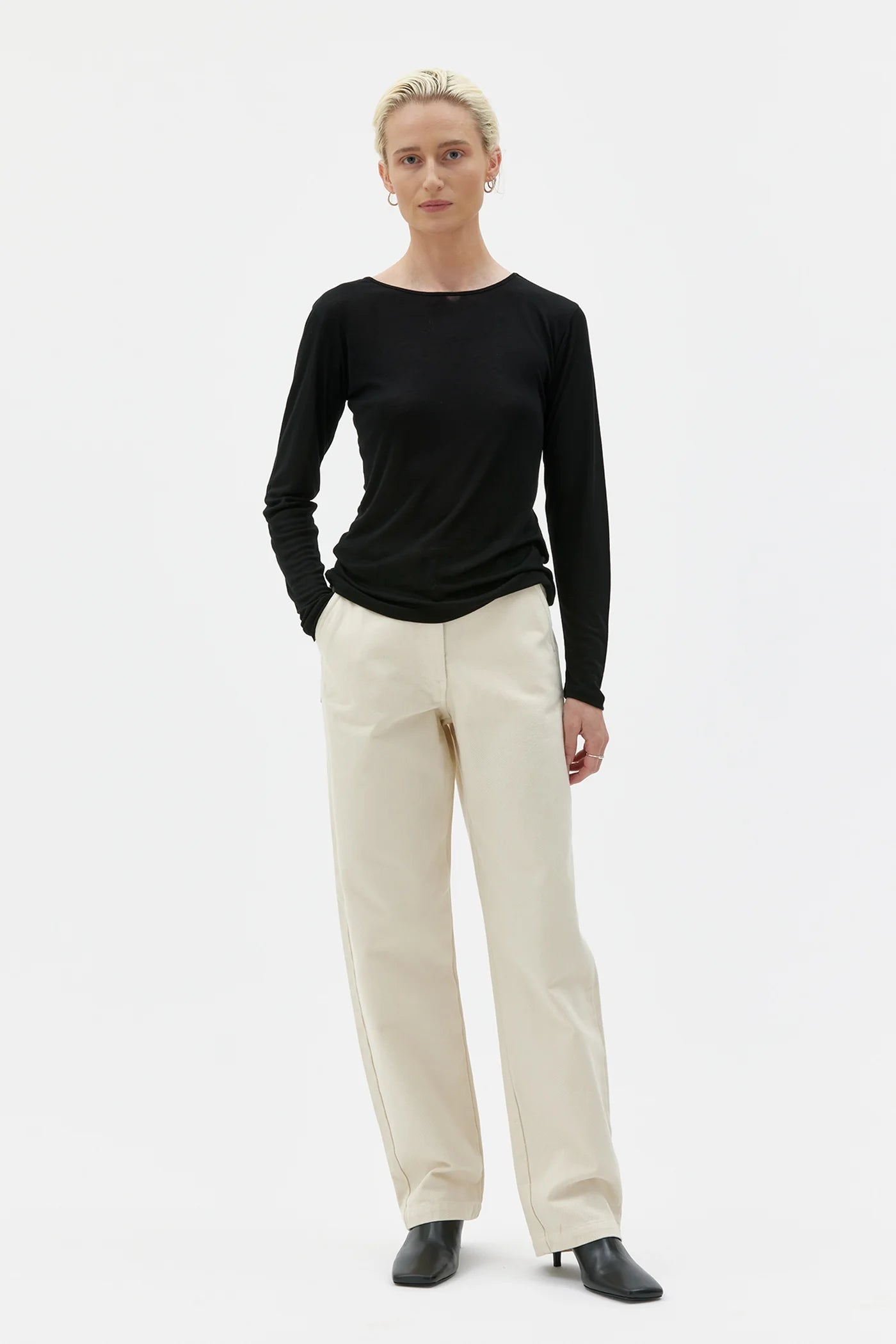 Person wearing a black long-sleeve top and beige pants on a white background