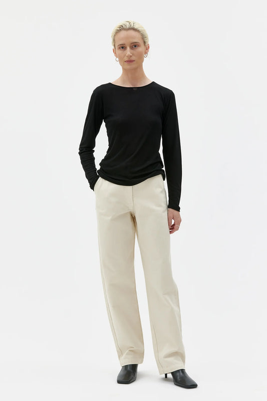 Person wearing a black long-sleeve top and beige pants on a white background
