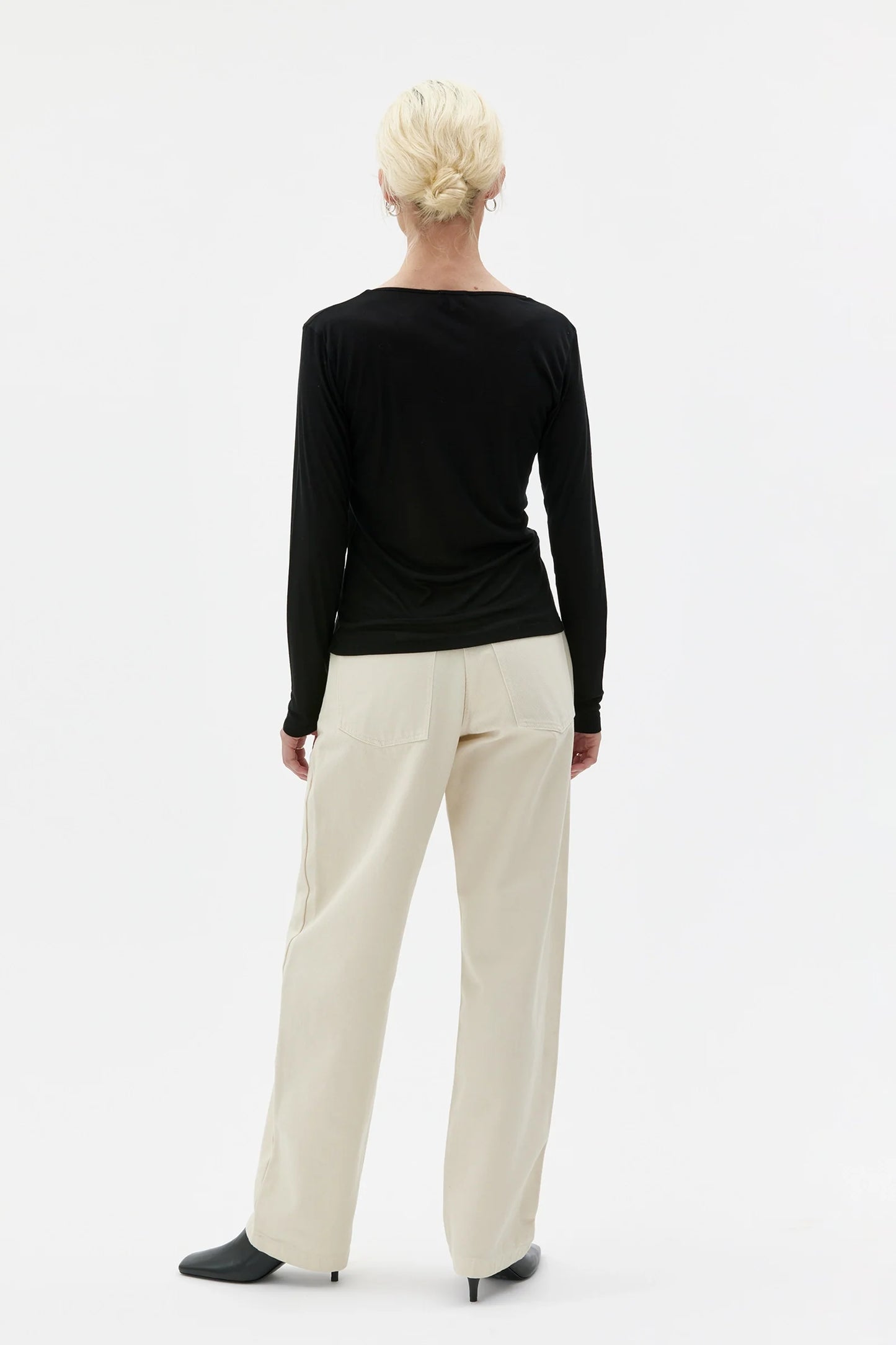 Person wearing a black long-sleeve top and white pants on a white background