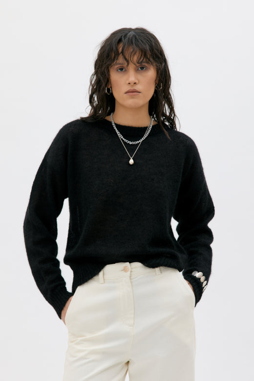 Woman wearing a black sweater and white pants against a white background
