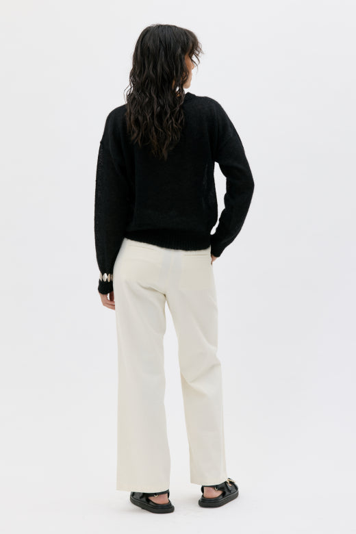 Person wearing a black sweater and white pants on a white background