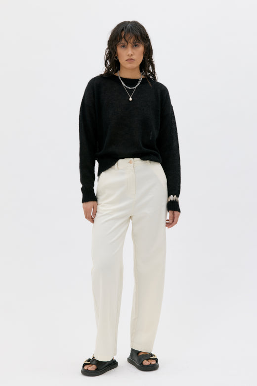 Person wearing a black sweater and white pants on a white background