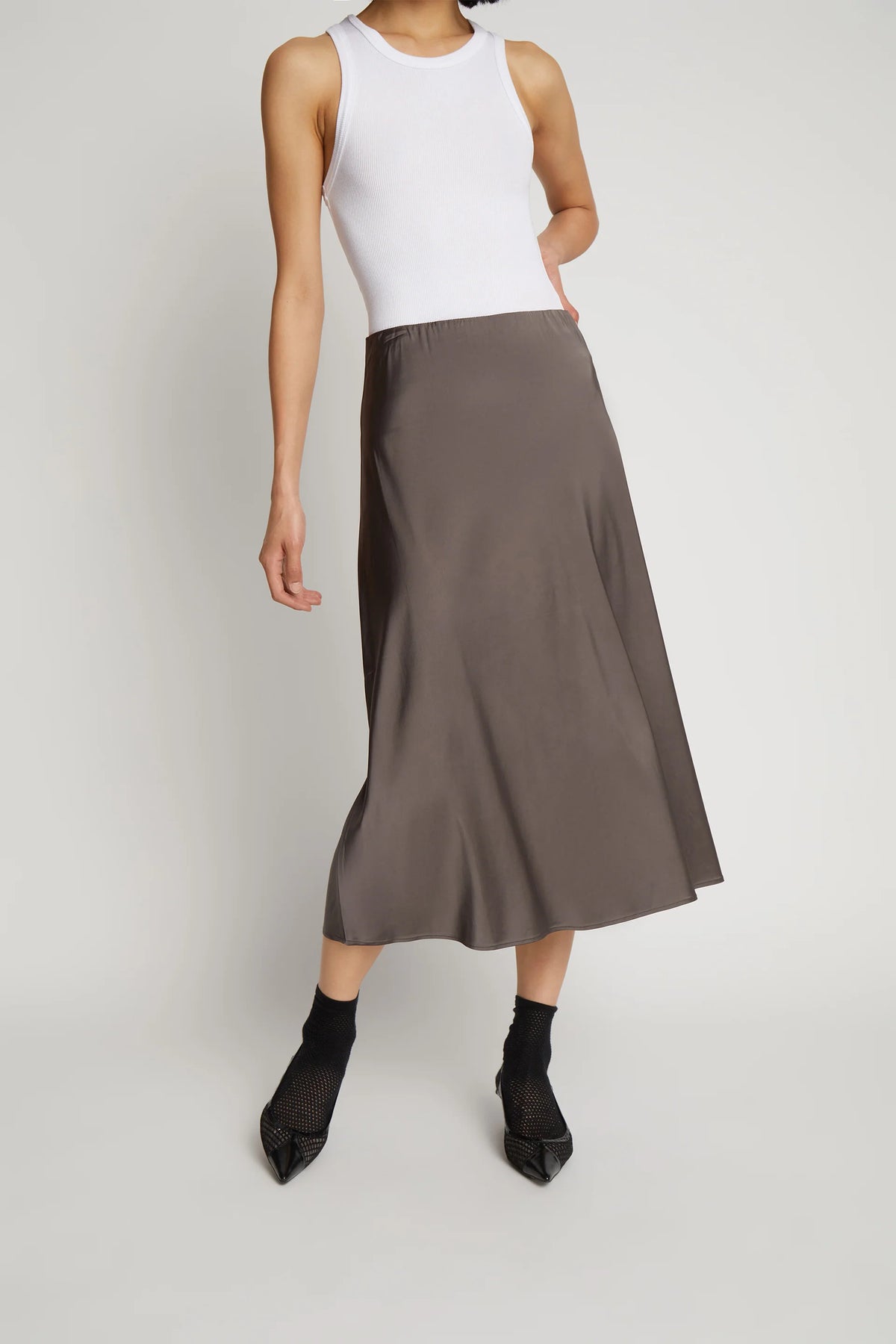 A model posing and wearing a long metallic grey skirt and a white top.