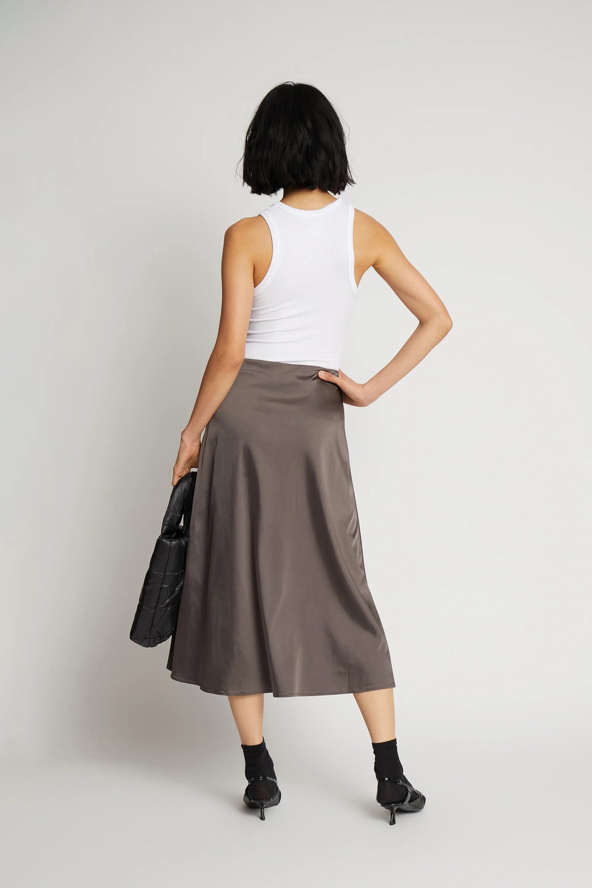A model posing and wearing a long metallic grey skirt and a white top.