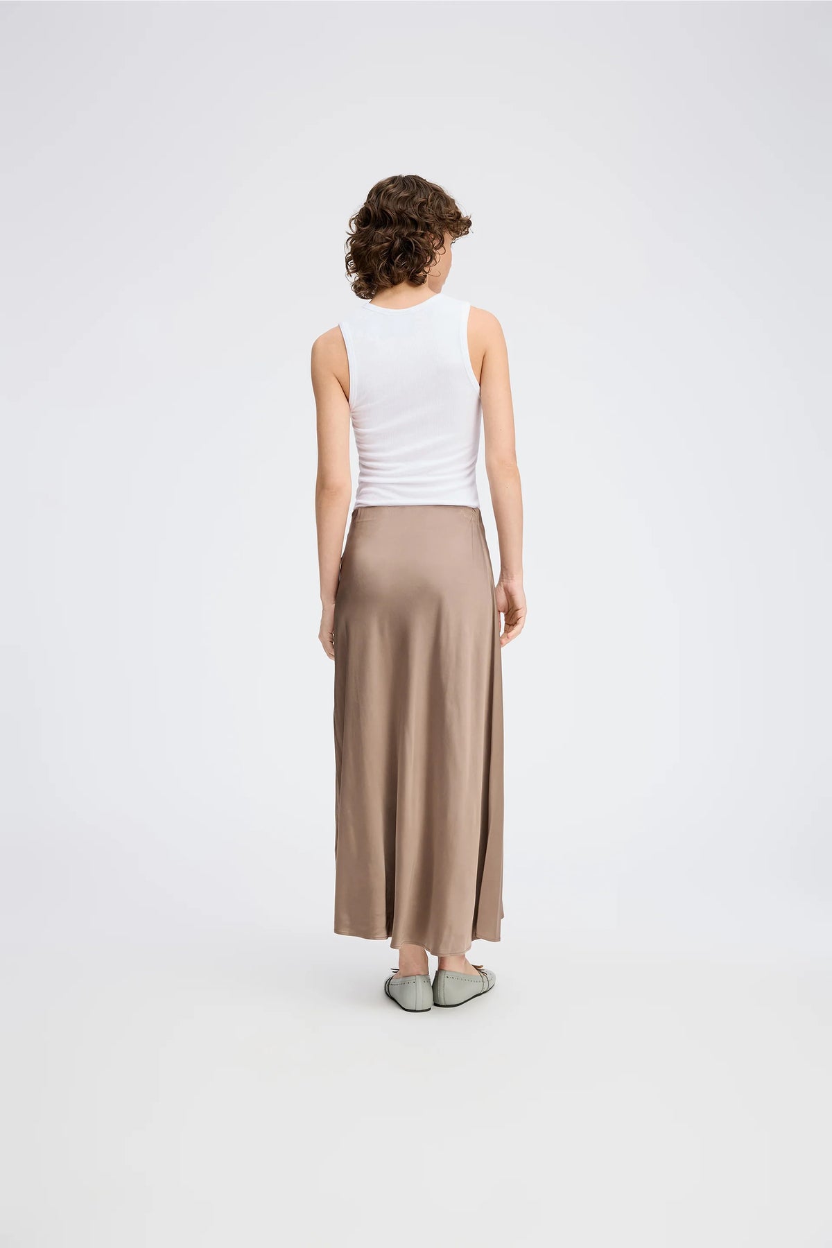 A posing model wearing a long camel color skirt and white top.