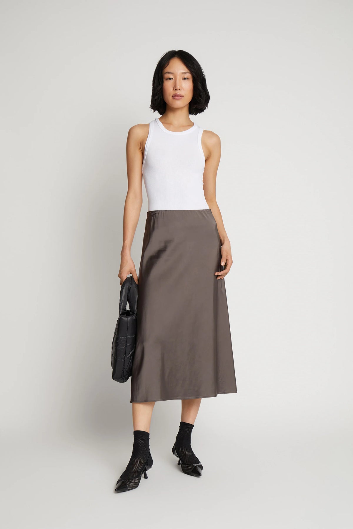 A model posing and wearing a long metallic grey skirt and a white top.