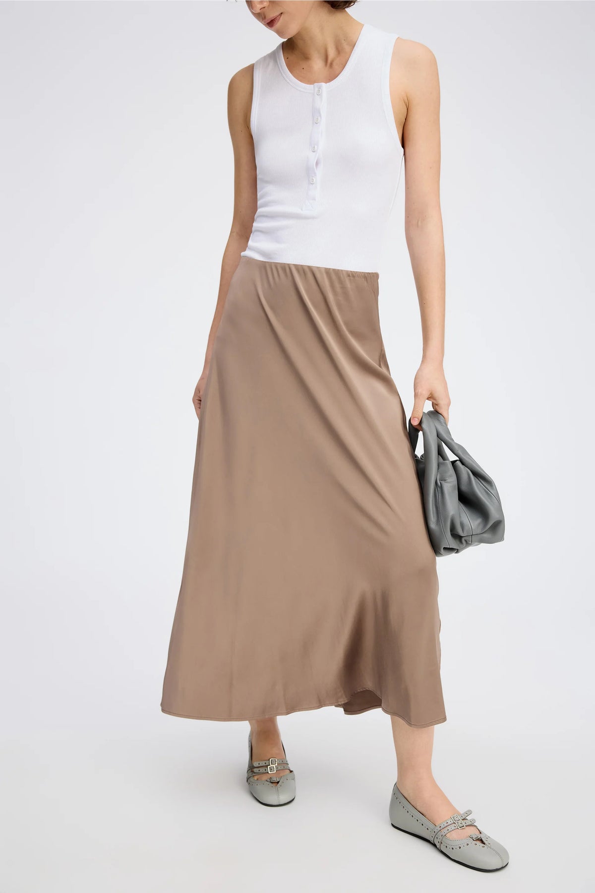 A posing model wearing a long camel color skirt and white top.