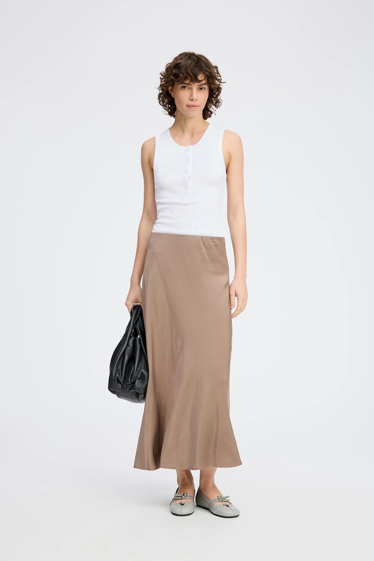 A posing model wearing a long camel color skirt and white top.
