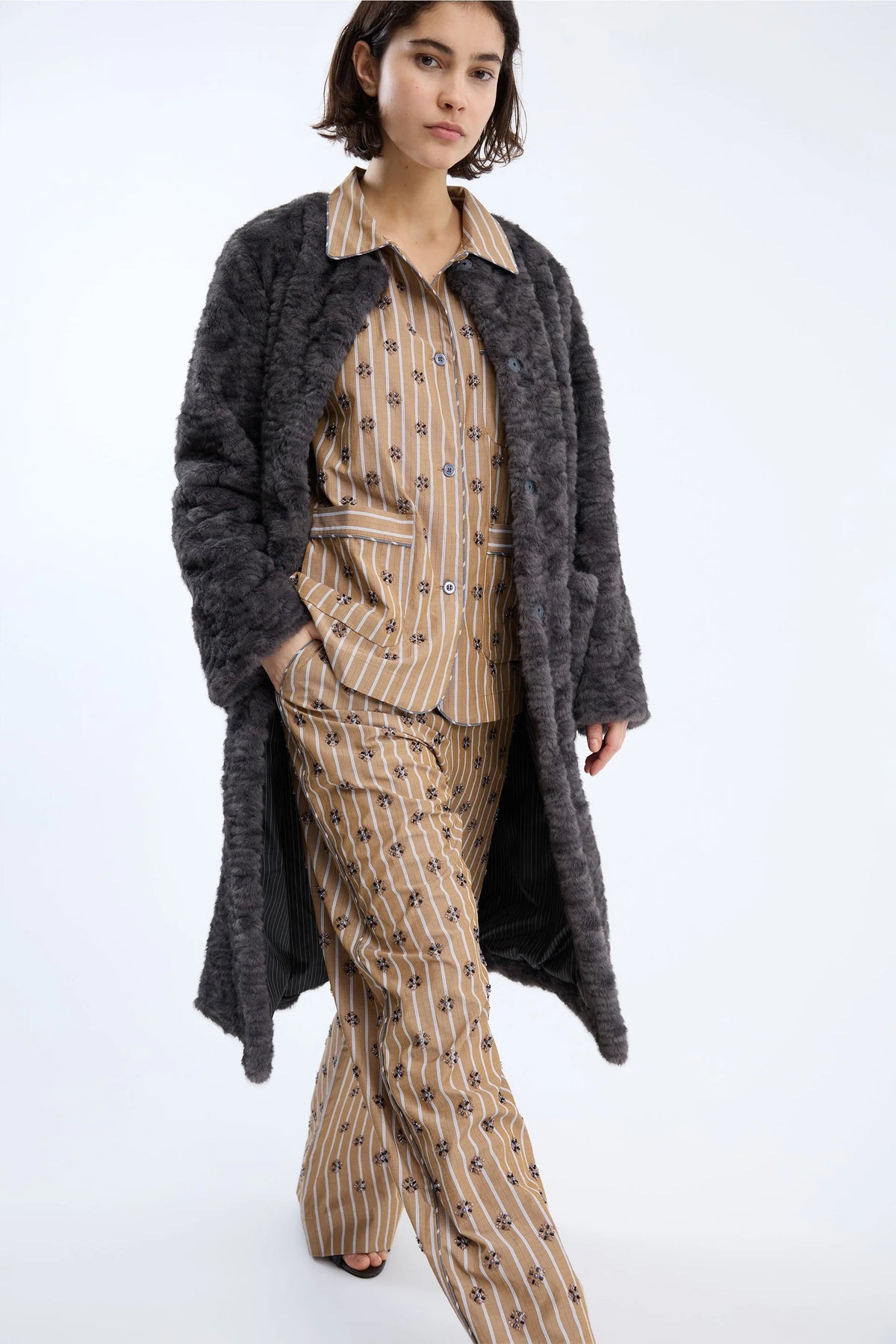 Woman wearing a long dark coat over a patterned outfit on a white background