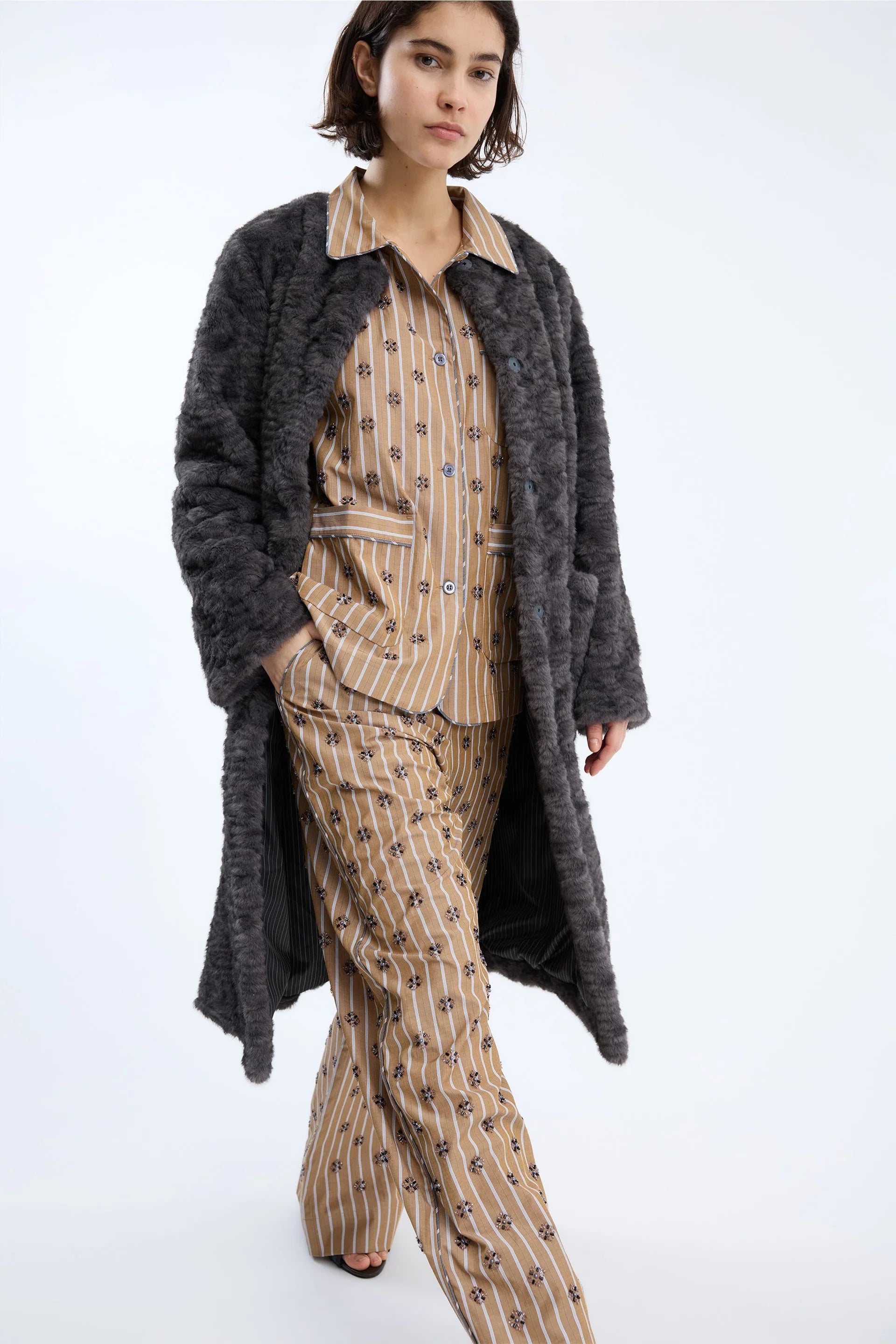 Woman wearing a long dark coat over a patterned outfit on a white background