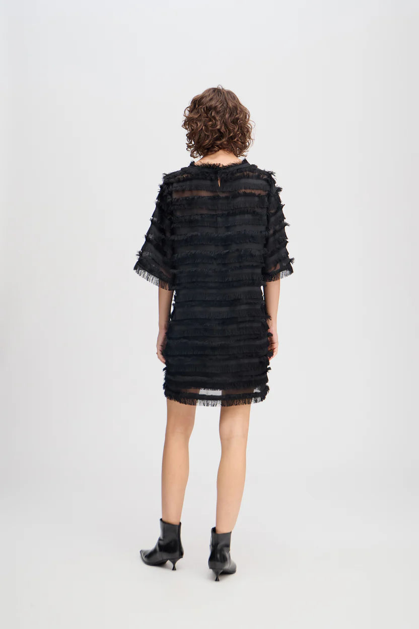 Person wearing a black dress with sheer sleeves on a white background