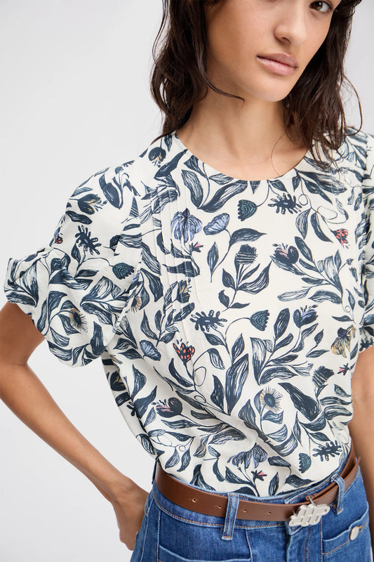 Woman wearing a white blouse with blue floral pattern and blue jeans on a plain background