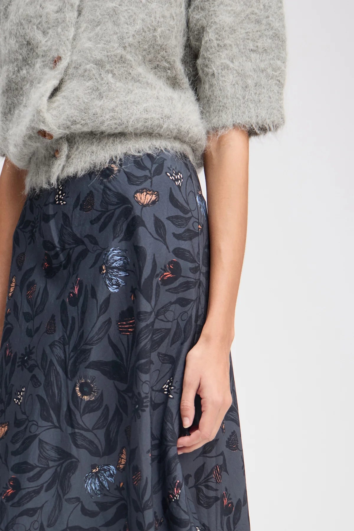Person wearing a gray sweater and dark floral skirt on a white background