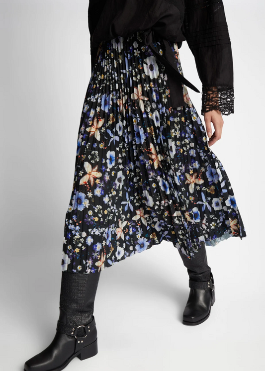 Lower body image of a model wearing a pleated floral print skirt with black background and blue, white and peach colored flowers. The skirt has an elastic waistband. The model is wearing black boots.