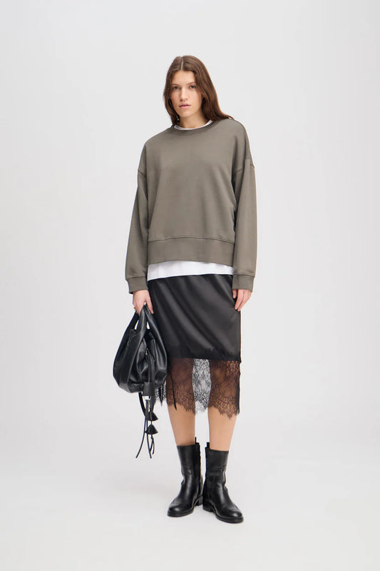 Person wearing a green sweater, black skirt, and black boots on a white background