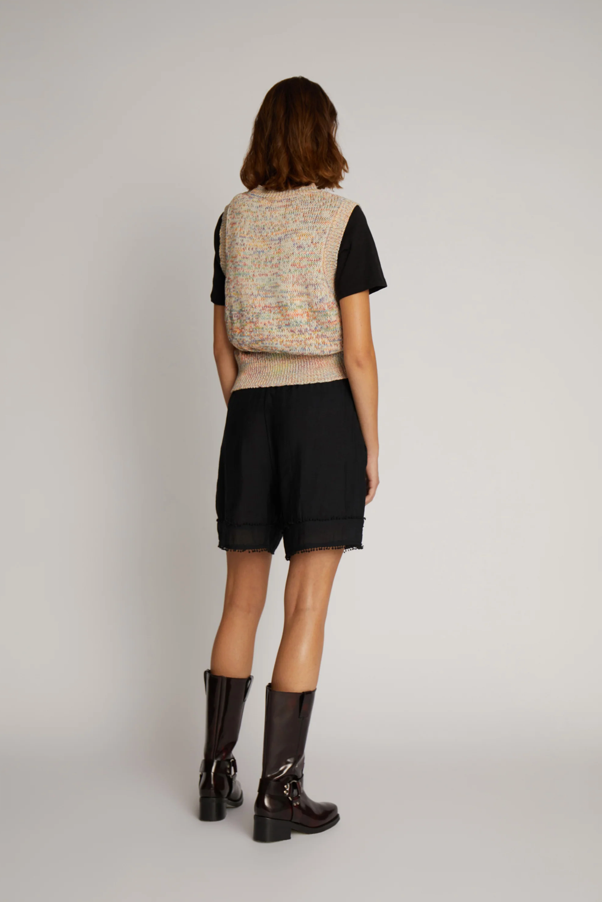 Reverse view of image of woman wearing black shorts and t-shirt with beige knitted vest