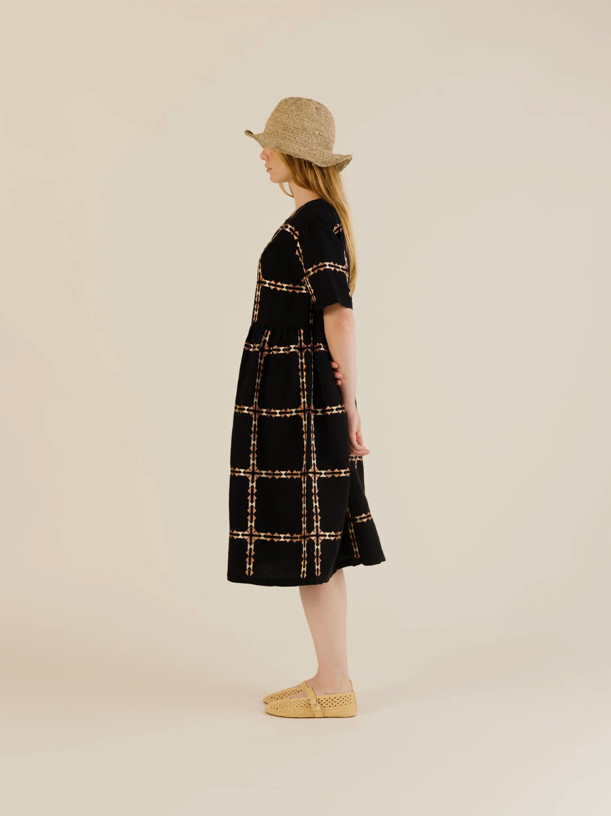 Woman wearing a black checkered dress and straw hat on a beige background