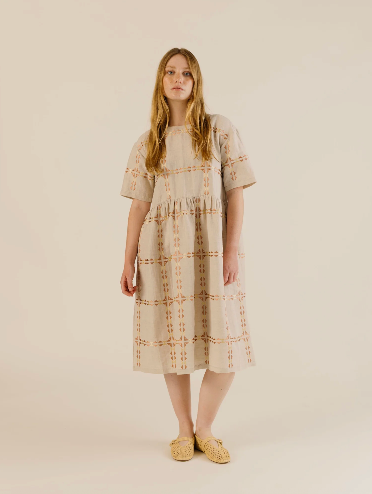 Woman wearing a beige dress with patterned details on a plain background