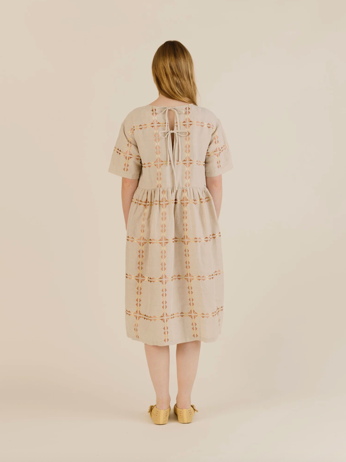 Woman wearing a beige embroidered dress on a plain background