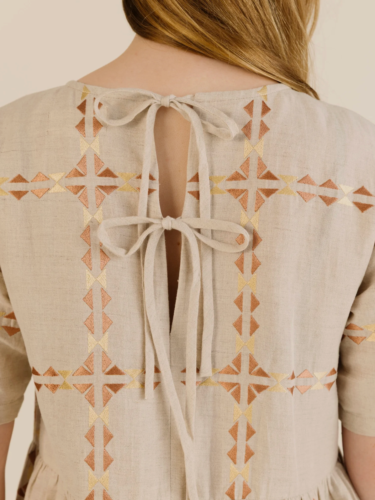 Beige dress with geometric pattern and bow detail on a plain background
