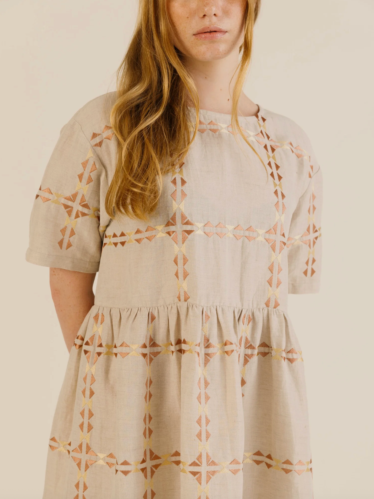 Woman wearing a beige dress with geometric patterns on a plain background
