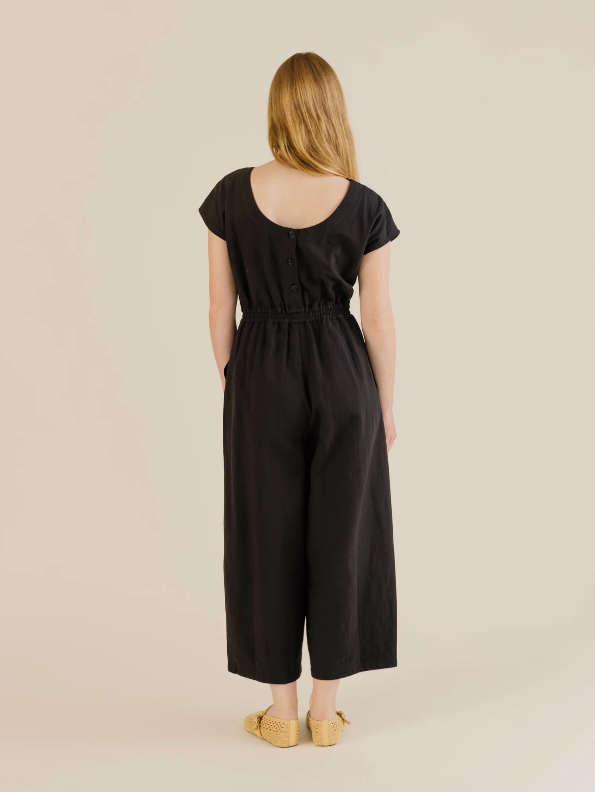 Woman wearing a black jumpsuit on a beige background
