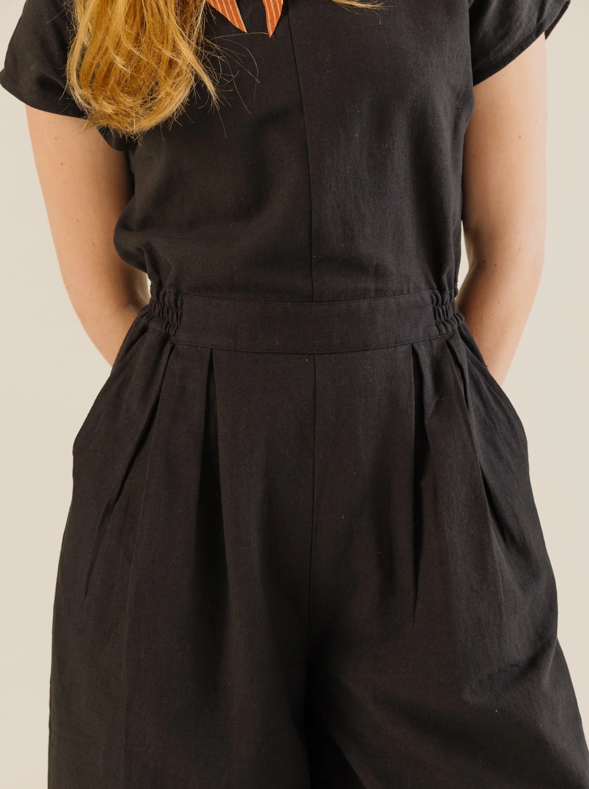 Person wearing a black sleeveless jumpsuit on a beige background