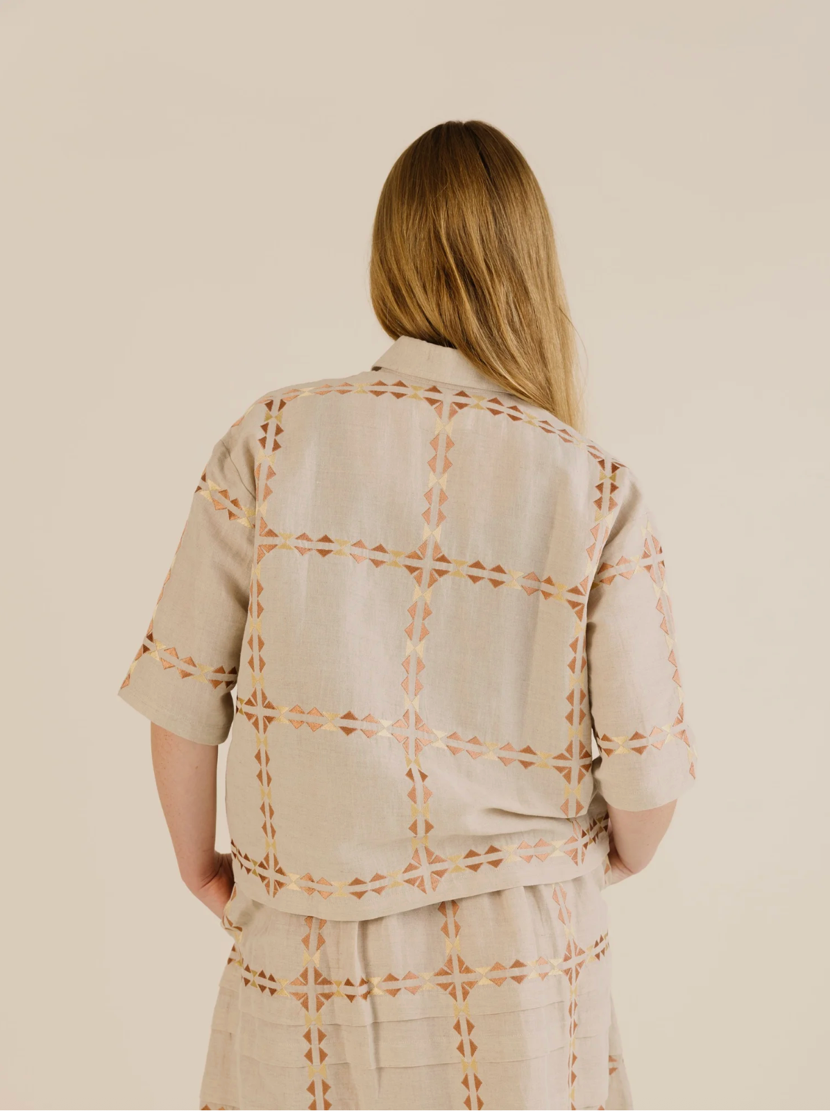 Person wearing a beige and brown patterned outfit on a plain background