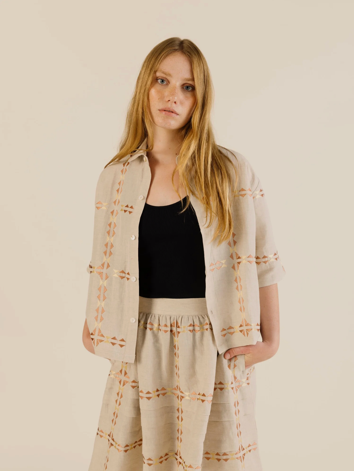 Woman wearing a beige patterned outfit against a plain background