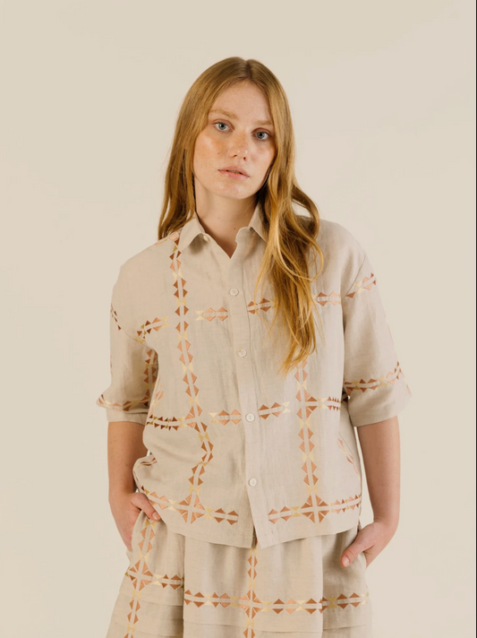 Woman wearing a beige embroidered shirt and pants against a plain background