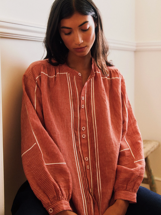 Woman wearing a rust-colored striped shirt sitting against a white wall.