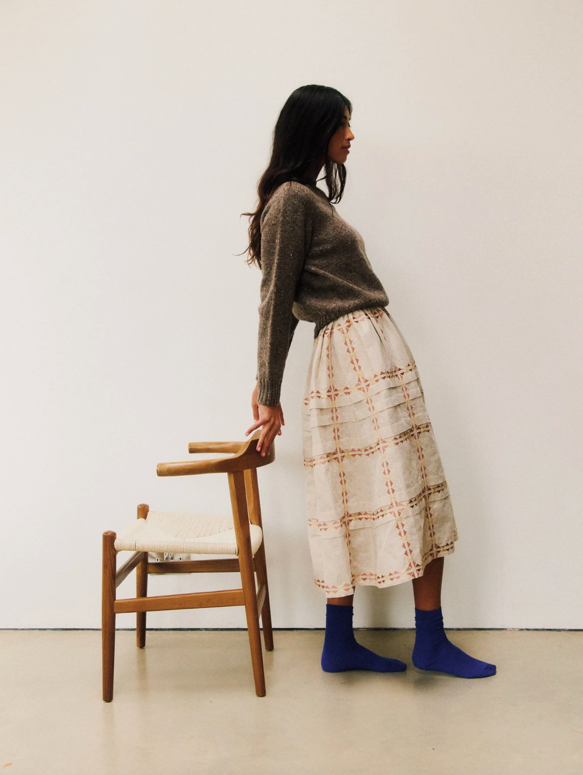 Woman standing next to a wooden chair against a white wall