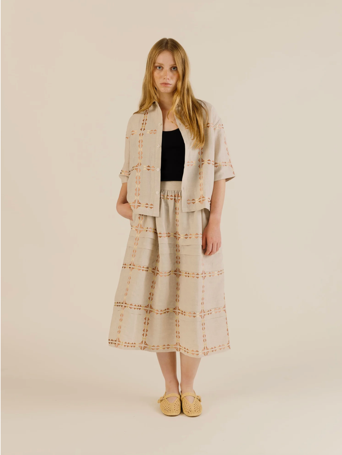 Woman wearing a beige plaid outfit with a black top on a plain background