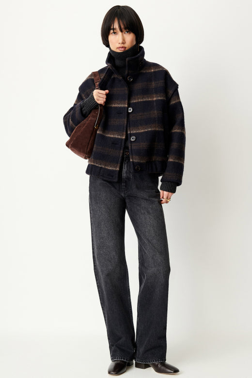 Person wearing a plaid jacket and jeans holding a brown bag on a white background