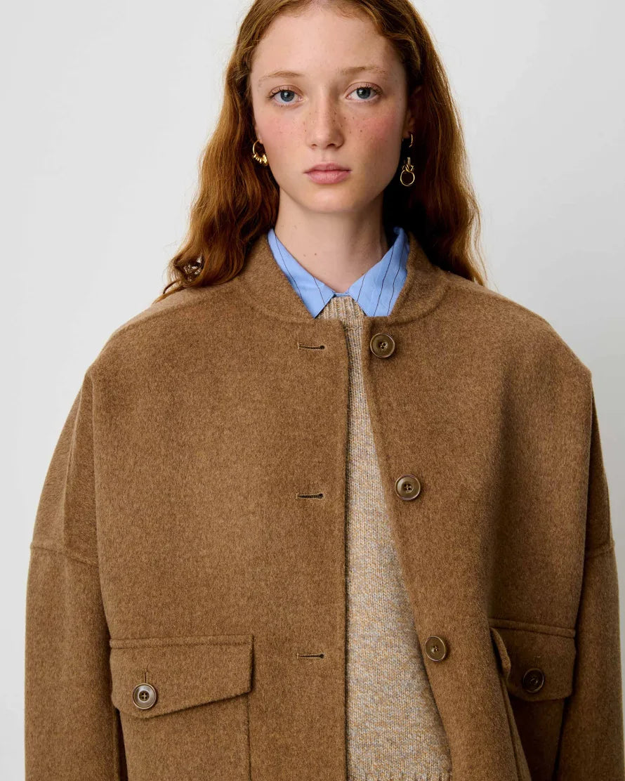A model shown wearing a light brown jacket over a blue shirt and knit vest.