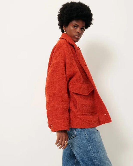 Person wearing a red textured jacket and blue jeans against a white background