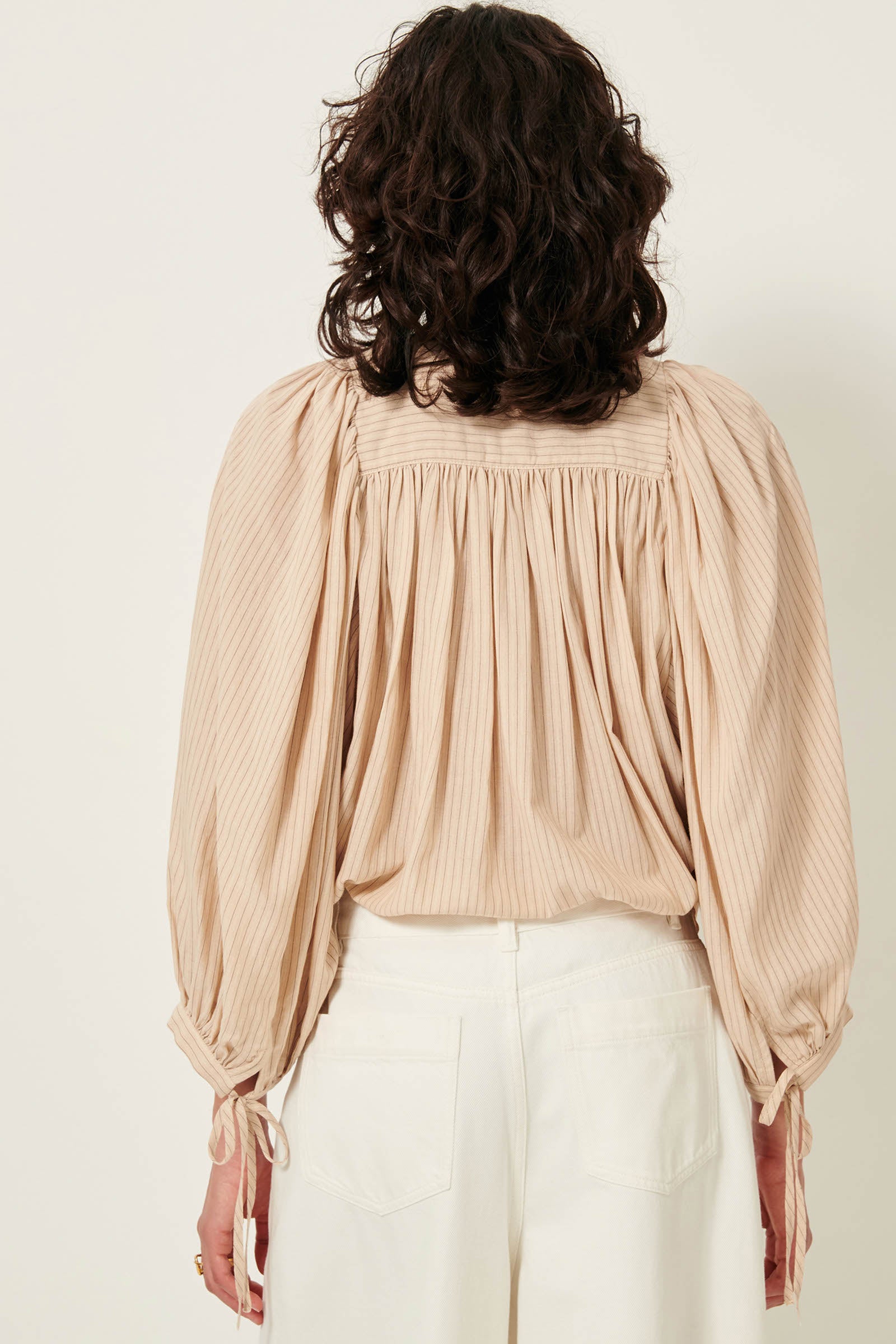 Picture of the back of a wavy brown haired young woman with brown eyes wearing a light brown striped shirt. 