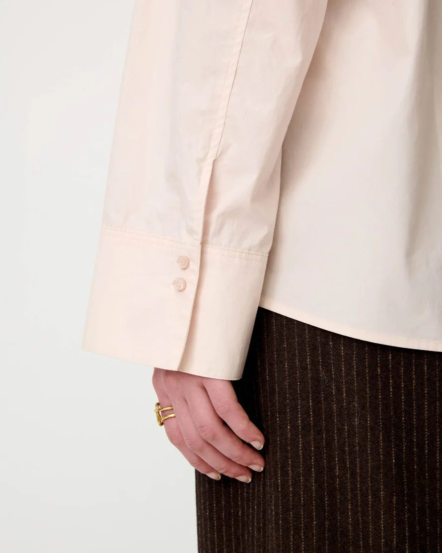 A close-up photo of the button detail of a light pink long sleeve shirt.