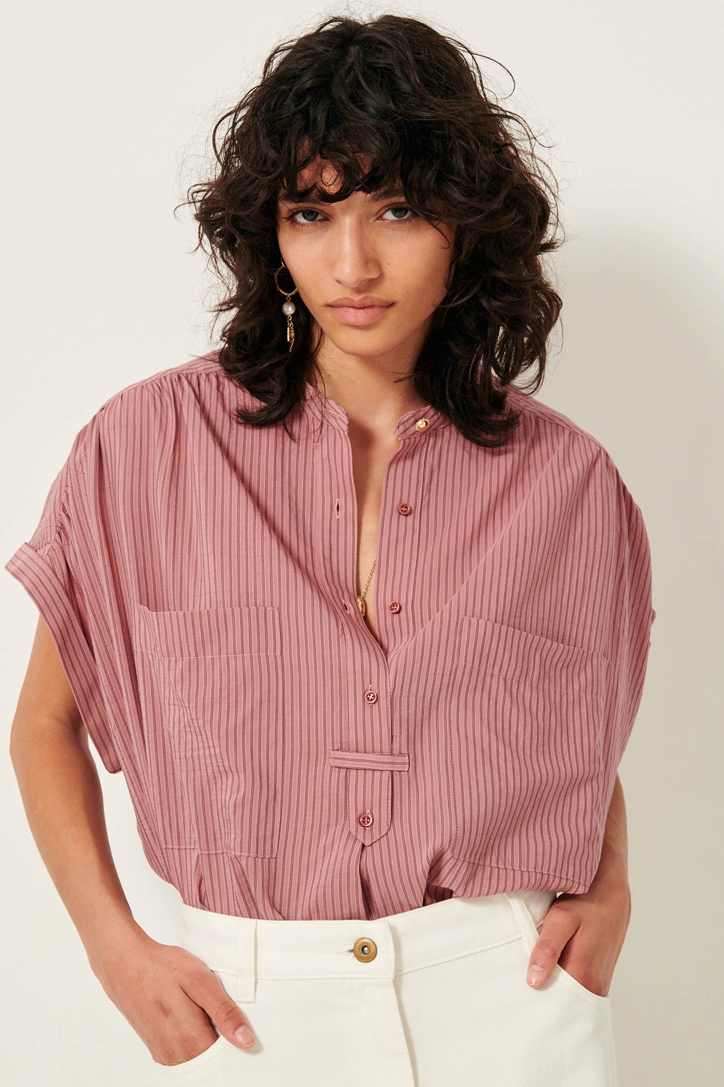 Picture of young women from the waist up with black wavy shoulder length hair dark brown eyes wearing a striped rose color sleeveless shirt.