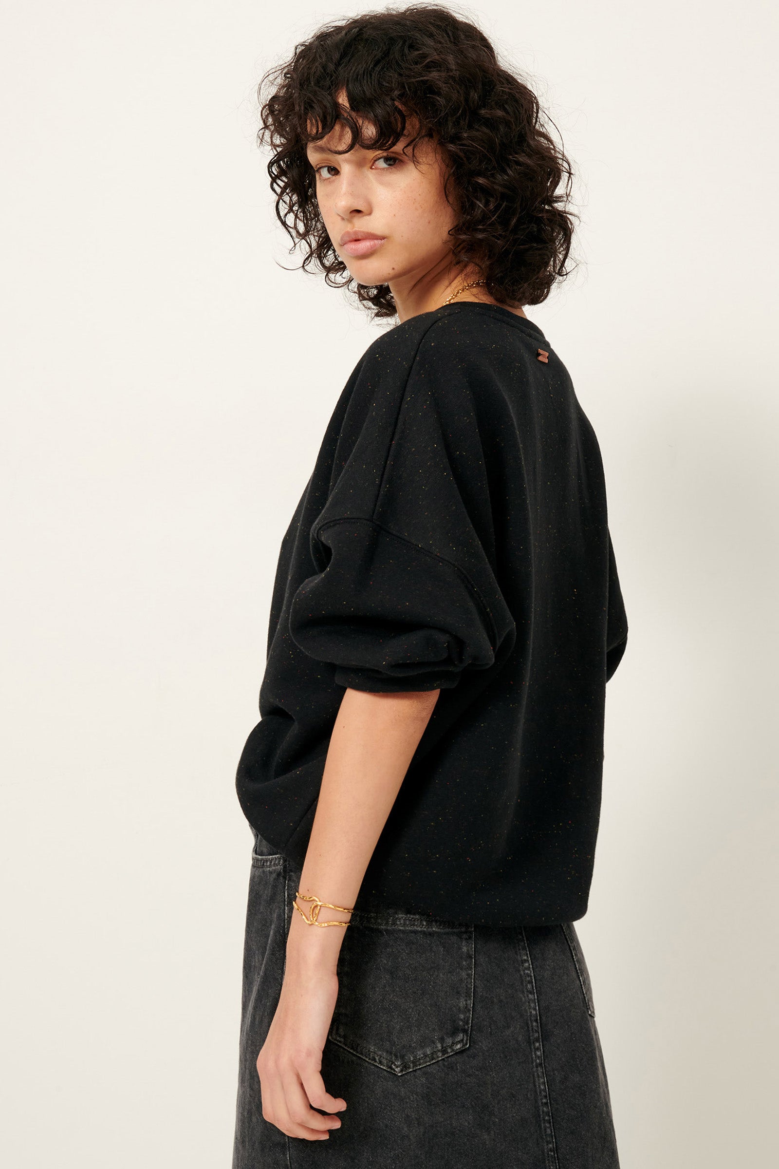 Side view of young woman with curly black hair wearing black sweatshirt and black denim skirt