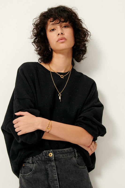 Picture of young woman with curly black hair wearing black sweatshirt and gold chain necklace