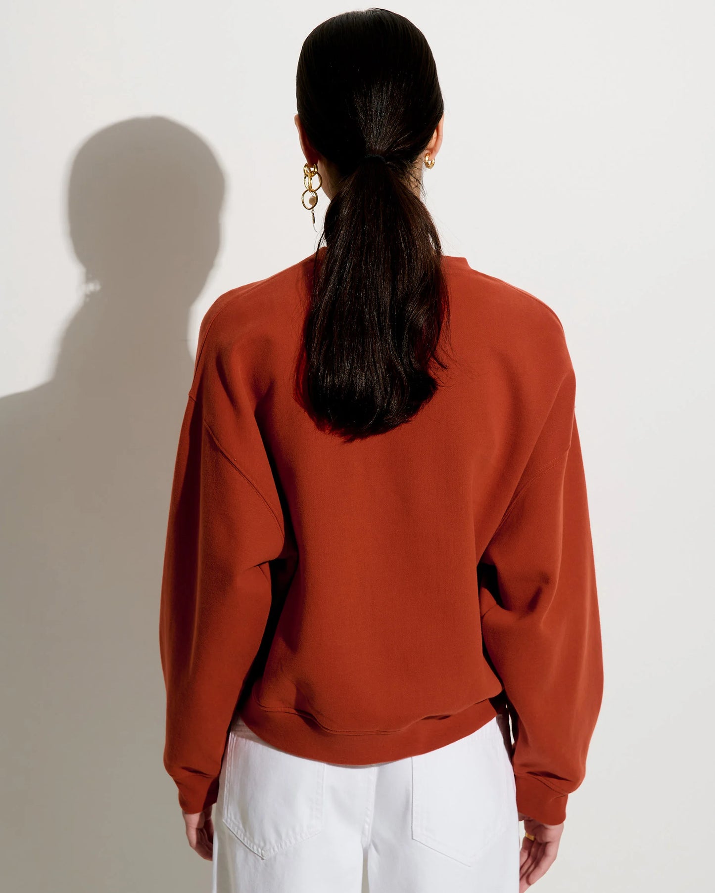 View from behind of a person wearing a rust-colored sweatshirt and white shorts against a plain background