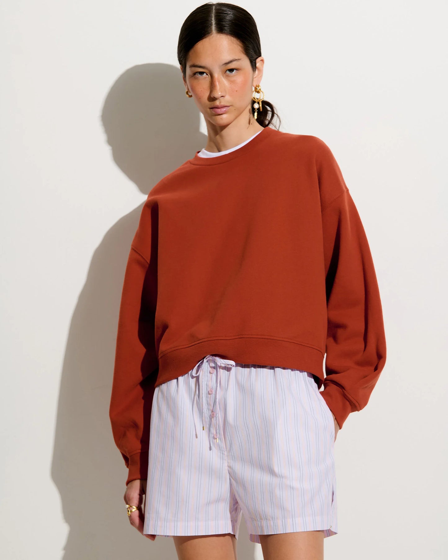Person wearing a rust-colored sweatshirt and white shorts against a plain background