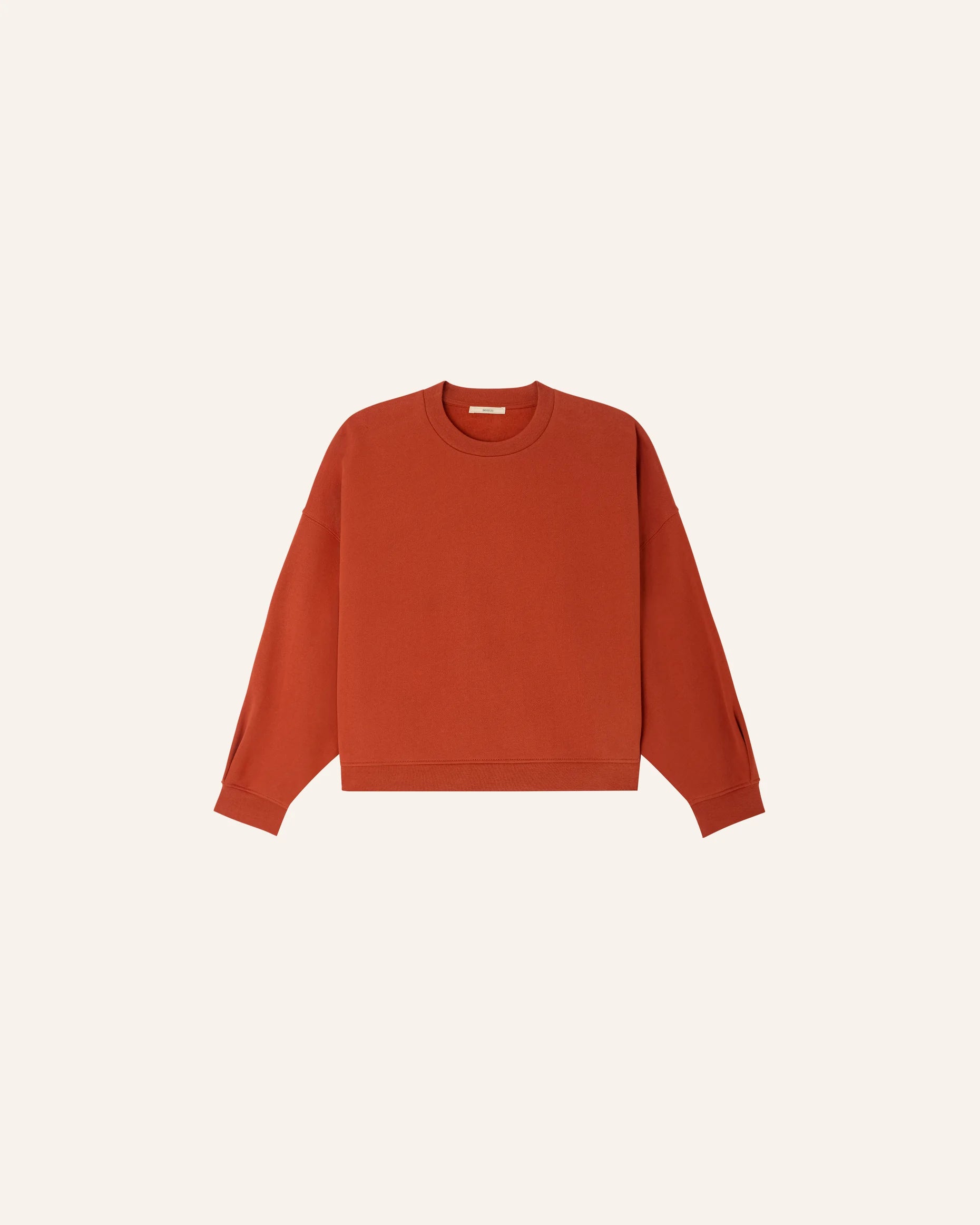 a rust-colored sweatshirt and white shorts against a plain background