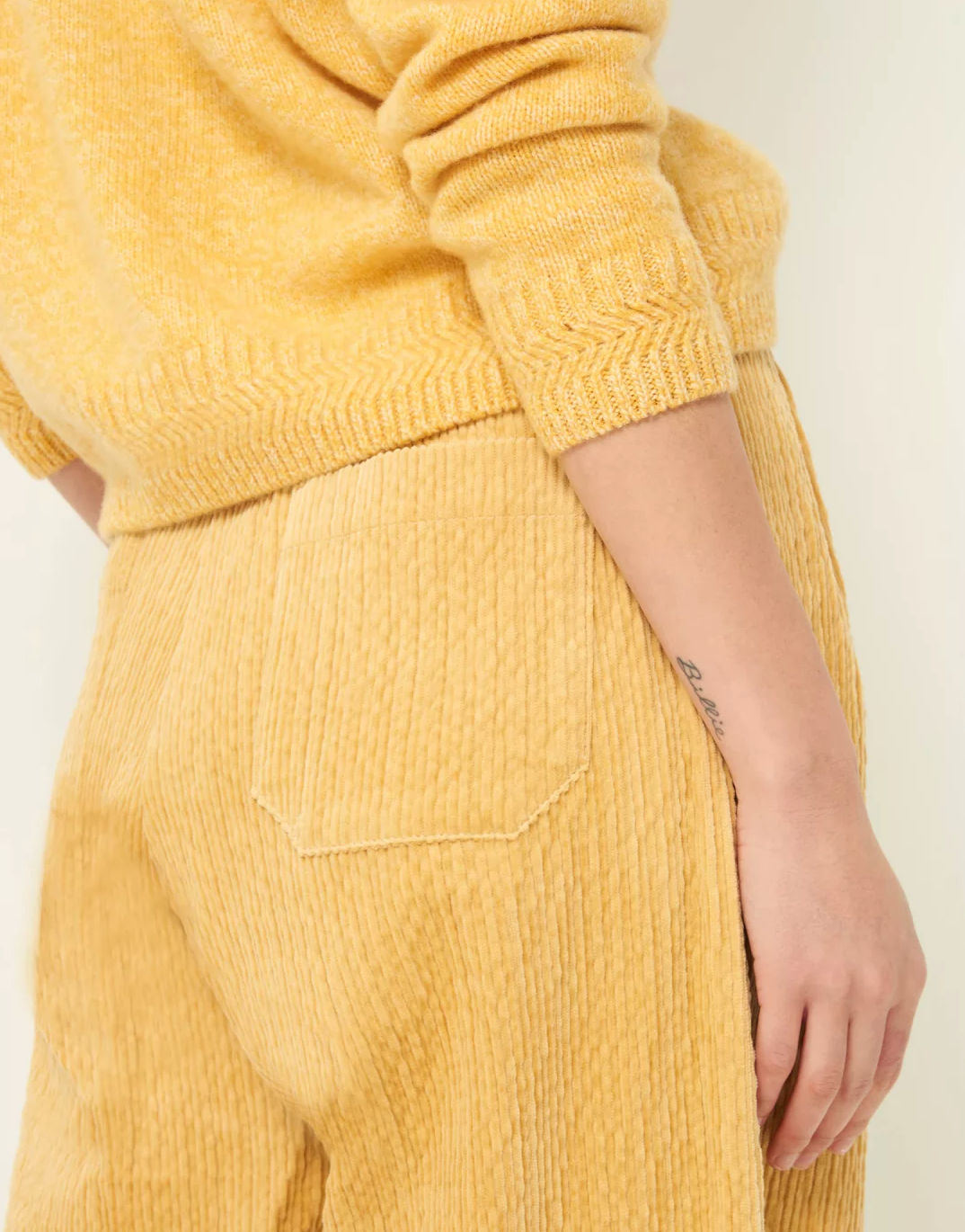 Partial back and side view of silty sweater with stitch detail around waist and cuff. Worn with yellow wide wale cord pants