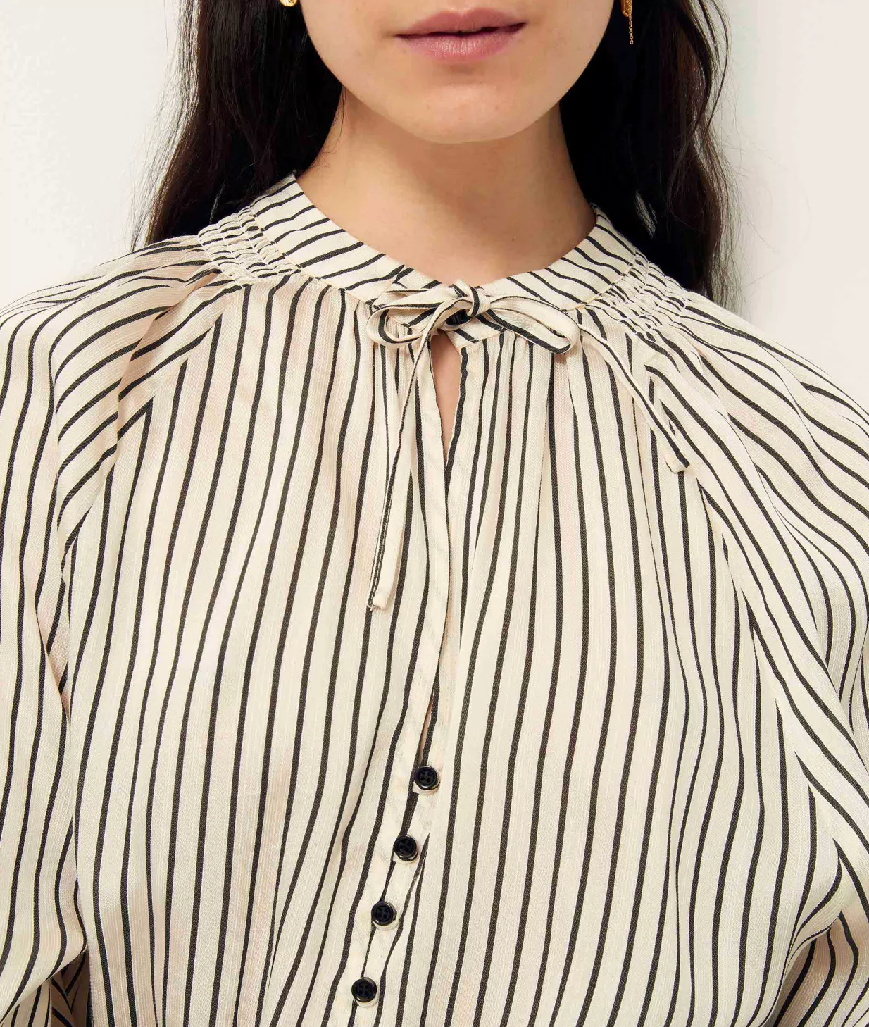 Front detail of stripe blouse tied with a small bow at the neckline. Buttoned at the front(showing 4 of the six buttons)